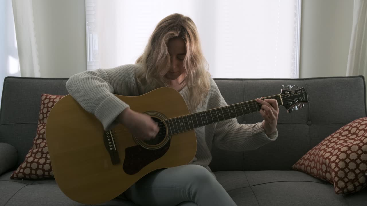 Attractive young blonde woman playing an acoustic guitar