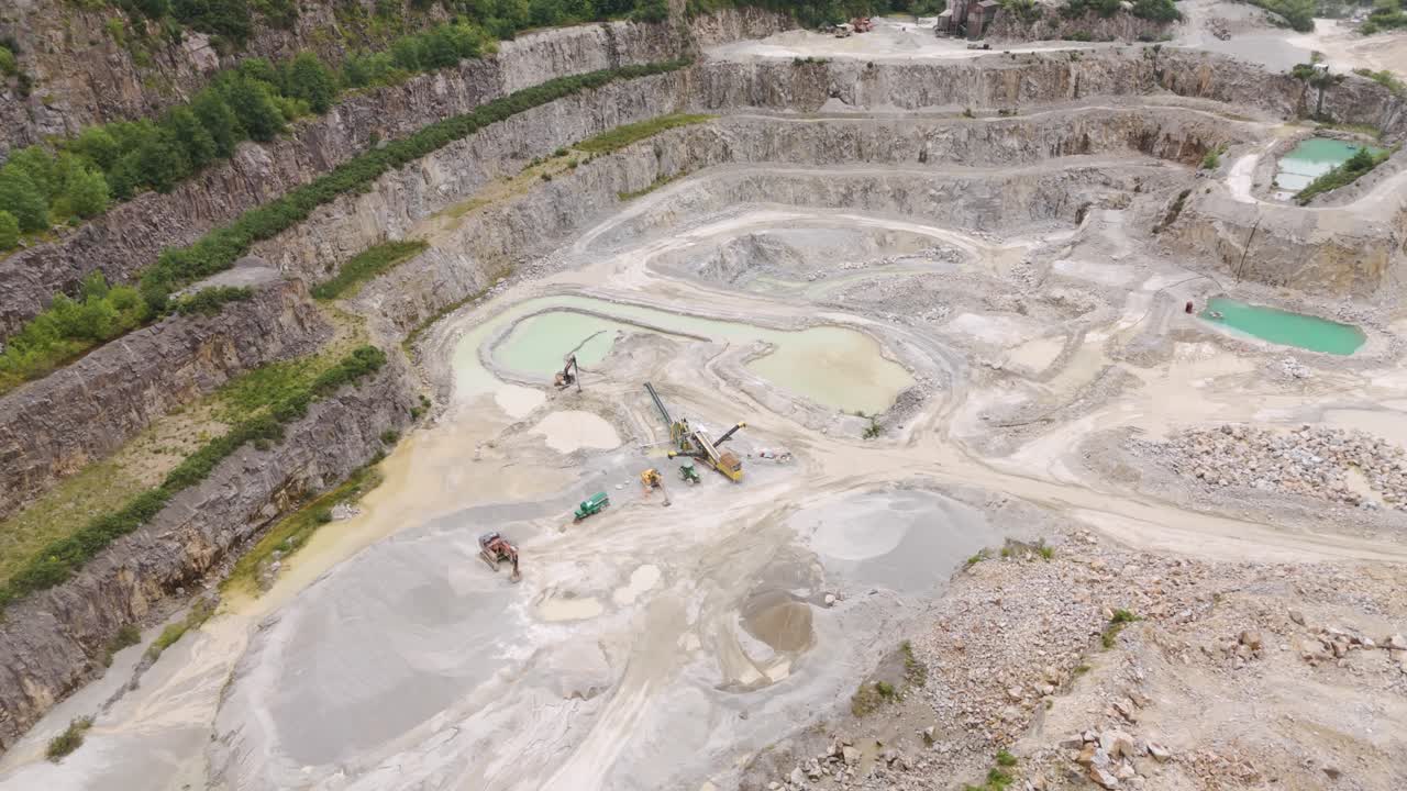 Orbital aerial view of machinery and earth-moving vehicles at the bottom of an aggregate quarry, capturing the industrial activity and equipment