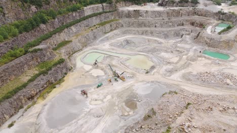 orbital aerial view of machinery and earth-moving vehicles at the bottom of an aggregate quarry, capturing the industrial activity and equipment