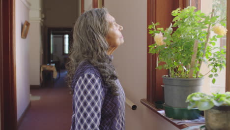 portrait of elderly woman walking to window looking curious in retirement home hallway background