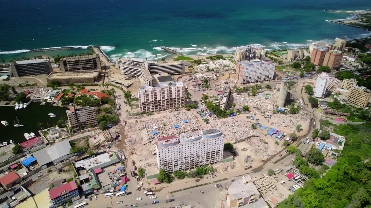 Angosciante prospettiva da drone che rivela l'entità della distruzione urbana, con edifici fratturati e detriti in contrasto con il porto intatto