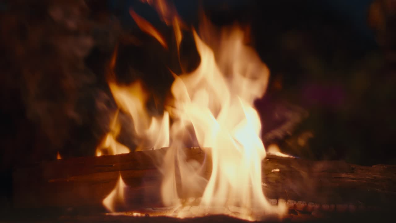 Il fuoco crepita calorosamente contro un cielo notturno buio. Le fiamme balzano e danzano sopra un mucchio di legna. Il fumo si arriccia delicatamente nell'aria fresca. Non sono visibili persone. Ideale per scene accoglienti, rustiche o notturne.