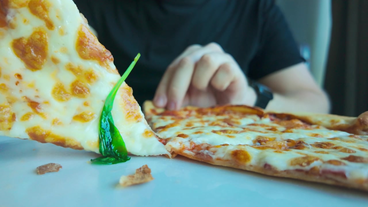 Ripresa ravvicinata, guarnizione di basilico fresco mentre una fetta di pizza si separa al rallentatore.