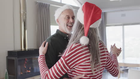 una pareja caucásica de mediana edad con sombreros de papá noel bailando en navidad en casa, en cámara lenta.