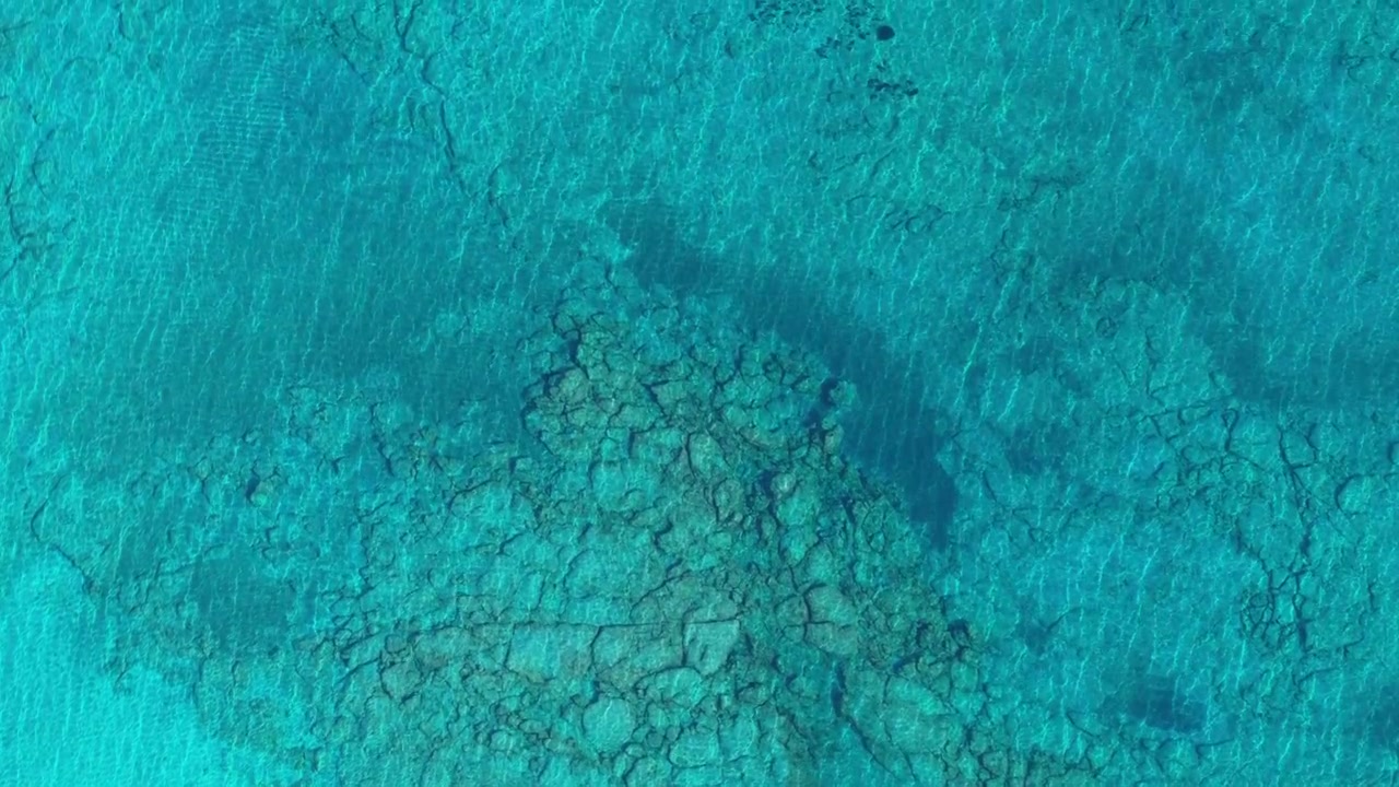 Drohnen-Luftaufnahme von oben von kristallklarem türkisfarbenem Wasser über einem felsigen Riffgrund, Kreta, Griechenland