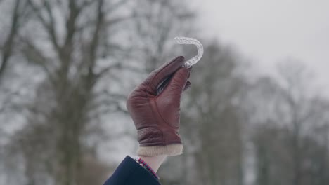 guante de cuero mano mostrando un alineador claro para la regulación de los dientes, día de invierno, de cerca