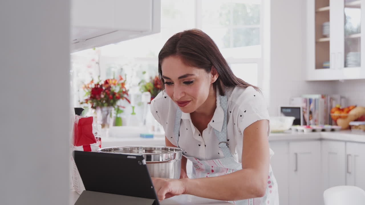 mujer hispana milenaria comprobando una receta en una tableta en su cocina, de cerca, ángulo bajo