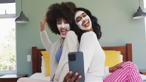 felices amigas diversas tomando selfies y sonriendo en el dormitorio