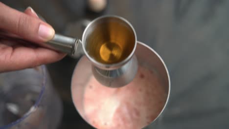 verter ron en una taza medidora haciendo un cóctel de granada usando jugo de granada fresco y semillas de ron jarabe de lima y ingredientes frescos