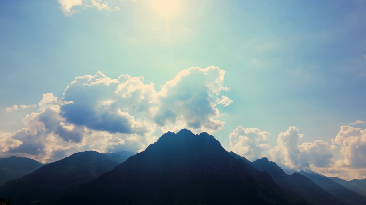 Dynamic backlit clouds above sharp mountain peak during sunny summer day. Riva di Solto, Italy (Riva di Solto, Italia)