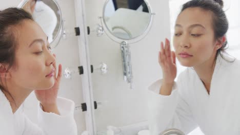 happy asian woman looking at mirror and touching face in bathroom, in slow motion