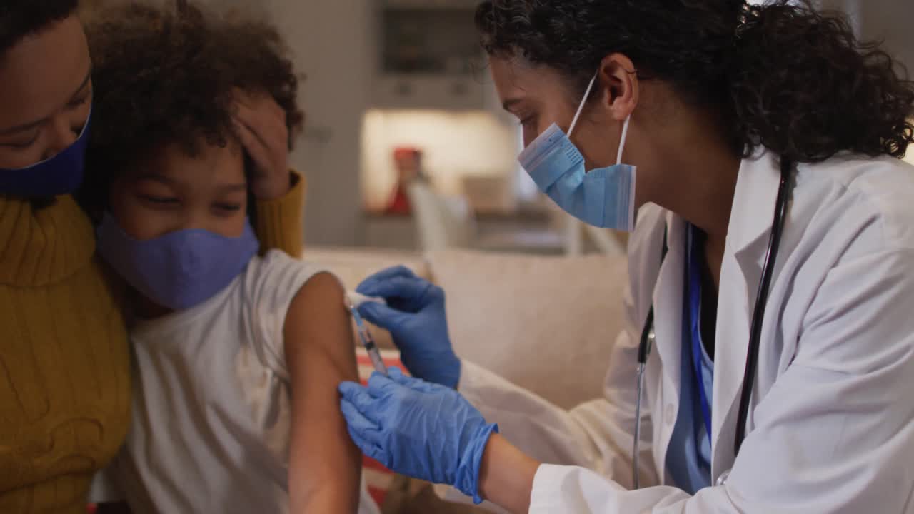 Médecin femme métisse portant un masque facial faisant une injection à la maison