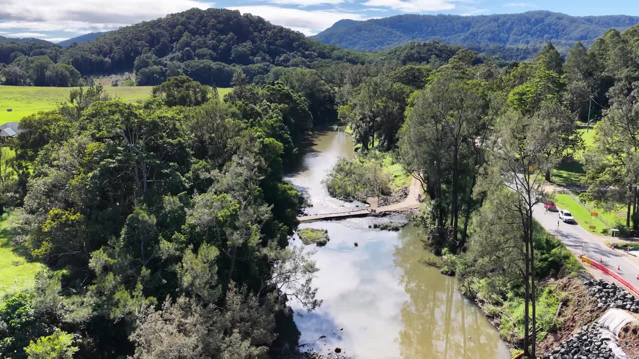 Aerial footage captures a serene river flowing through lush forests under bright daylight, showcasing natural beauty and tranquility