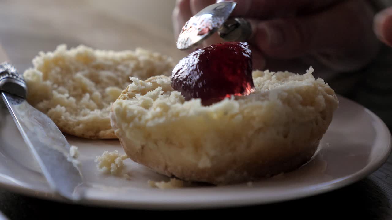 cucharas de mano cucharada de mermelada en bollos tradicionales al vapor recién horneados y coloca el cuchillo en un plato blanco durante el té de la tarde