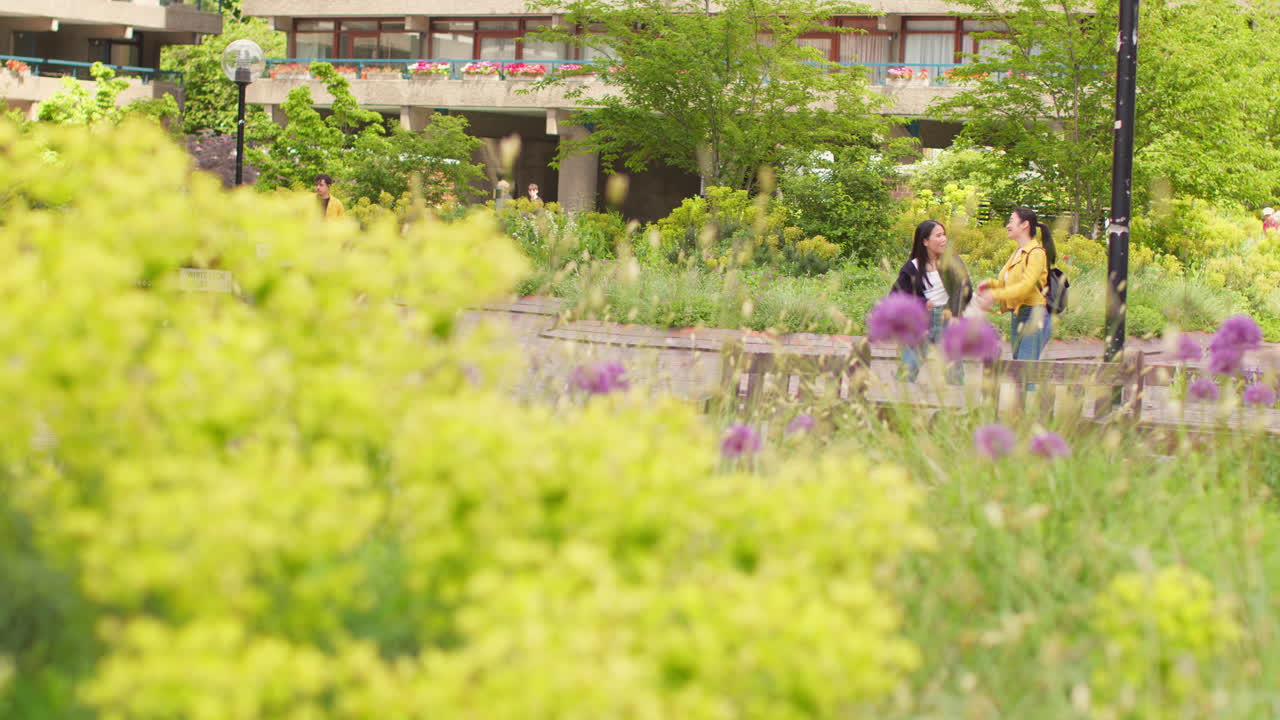 두 명의 미소 짓는 젊은 여성 친구가 실시간으로 도시 거리를 따라 야외에서 는 동안 대화하는 광각 시각