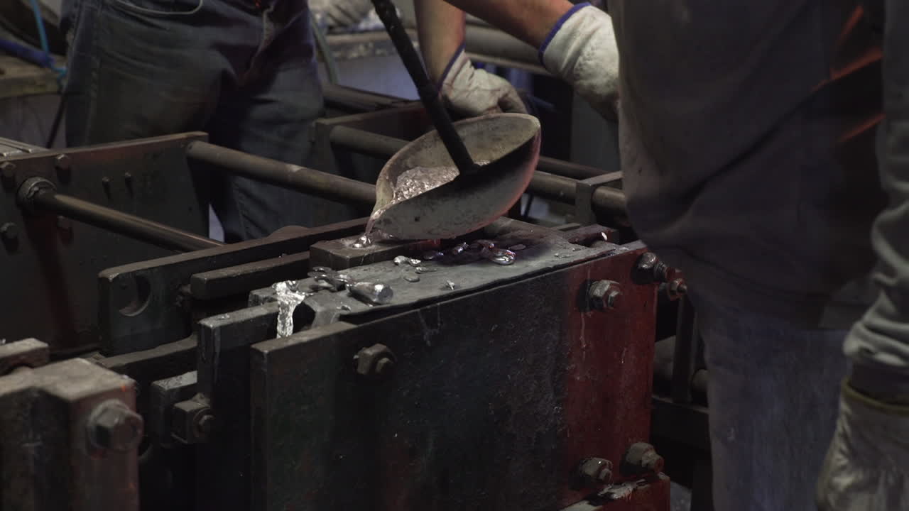 gente vertiendo metal fundido en moldes en una fábrica