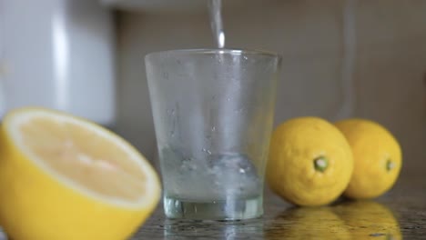 pouring lemonade and ice cubes into glass between lemons splashing countertop