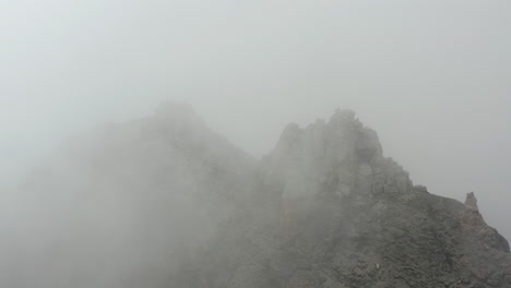 flying over rocky mountain summit covered in thick mist