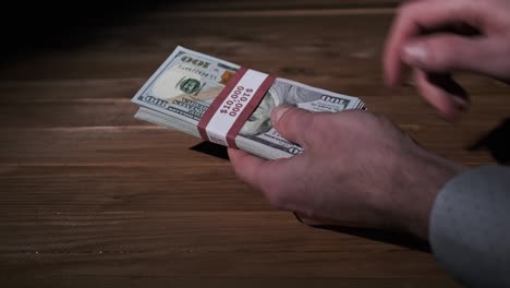 una pila de billetes de 10.000 dólares estadounidenses en manos masculinas sobre un fondo de madera.