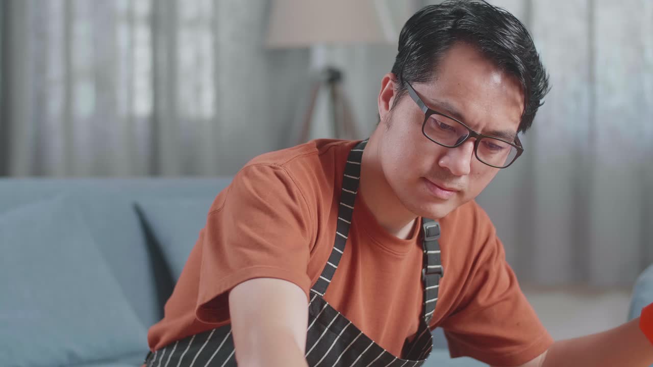 집에서 스프레이로 테이블을 청소하는 아프론을 입은 아시아 남성 집무원