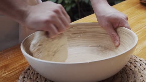 Chef-molds-the-pizza-dough-in-a-deep-plate,-on-a-wooden-table