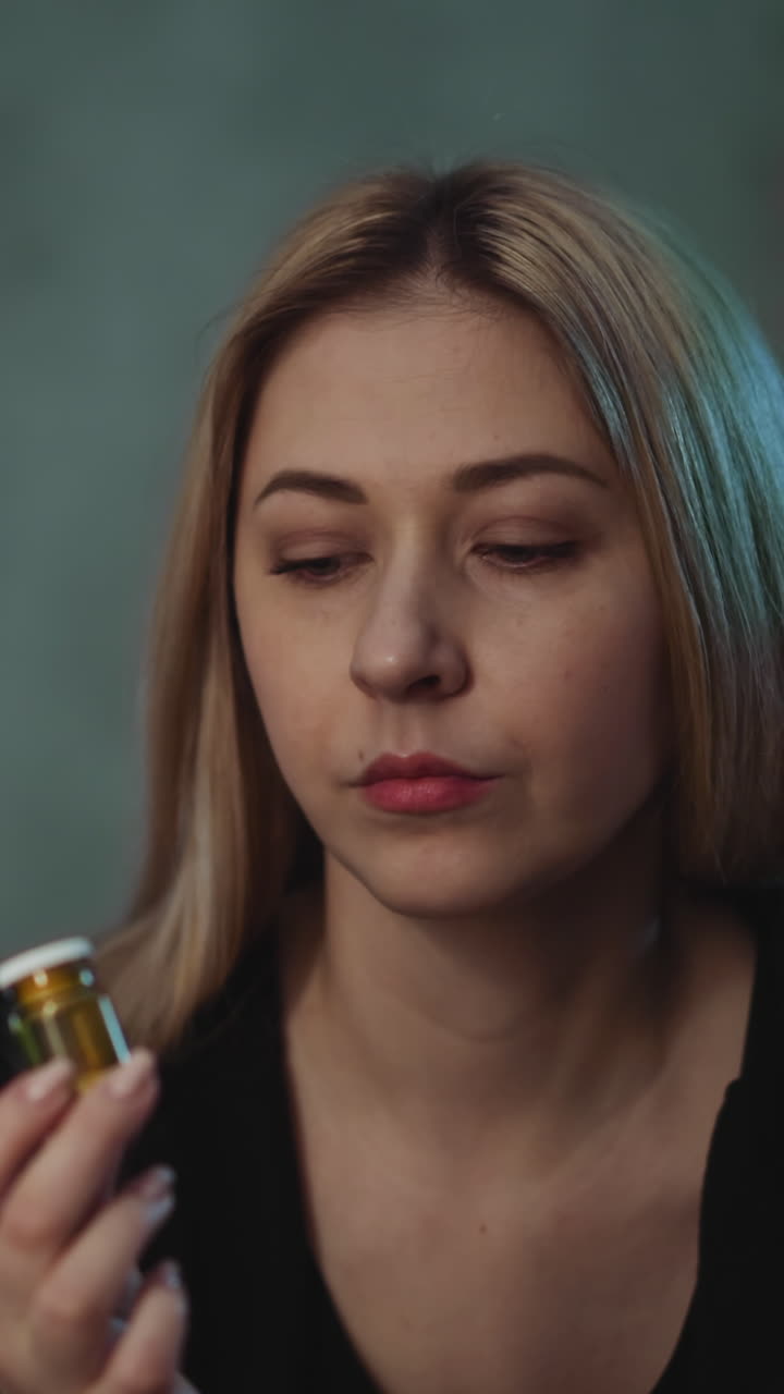 una mujer reflexiva gira una botella de vidrio de medicamentos con productos nutricionales no registrados dudando de la receta del médico en una habitación semi-oscura en primer plano en cámara lenta