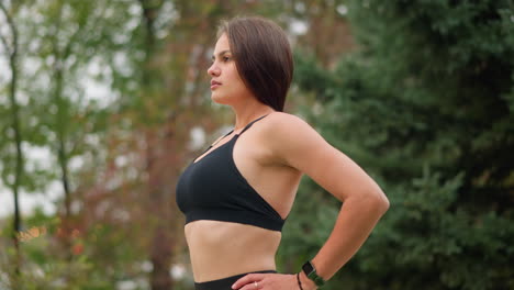 girl outdoor in black singlet standing and breathing in deeply with hand on waist, calm and focused expression, healthy posture, feeling refreshed, natural beauty, fitness moment, outdoor breath