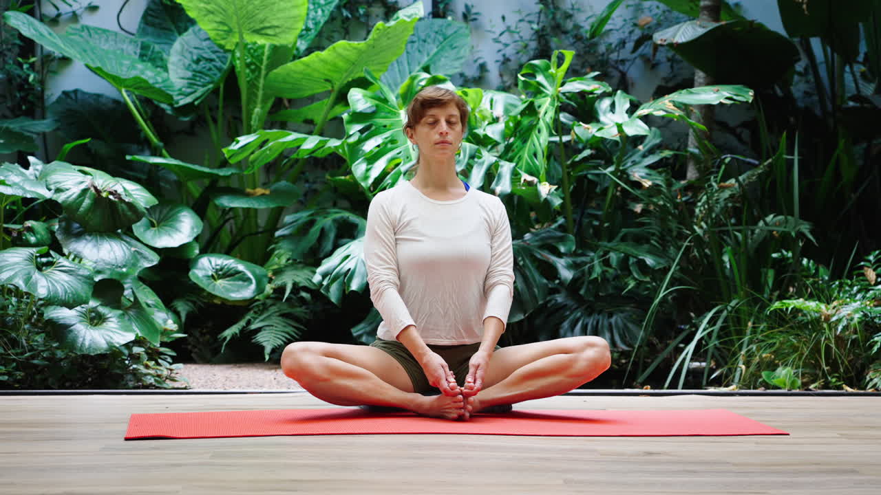 Mulher Meditando em Posição de Yoga no Tapete Rodeada por Plantas Verdes