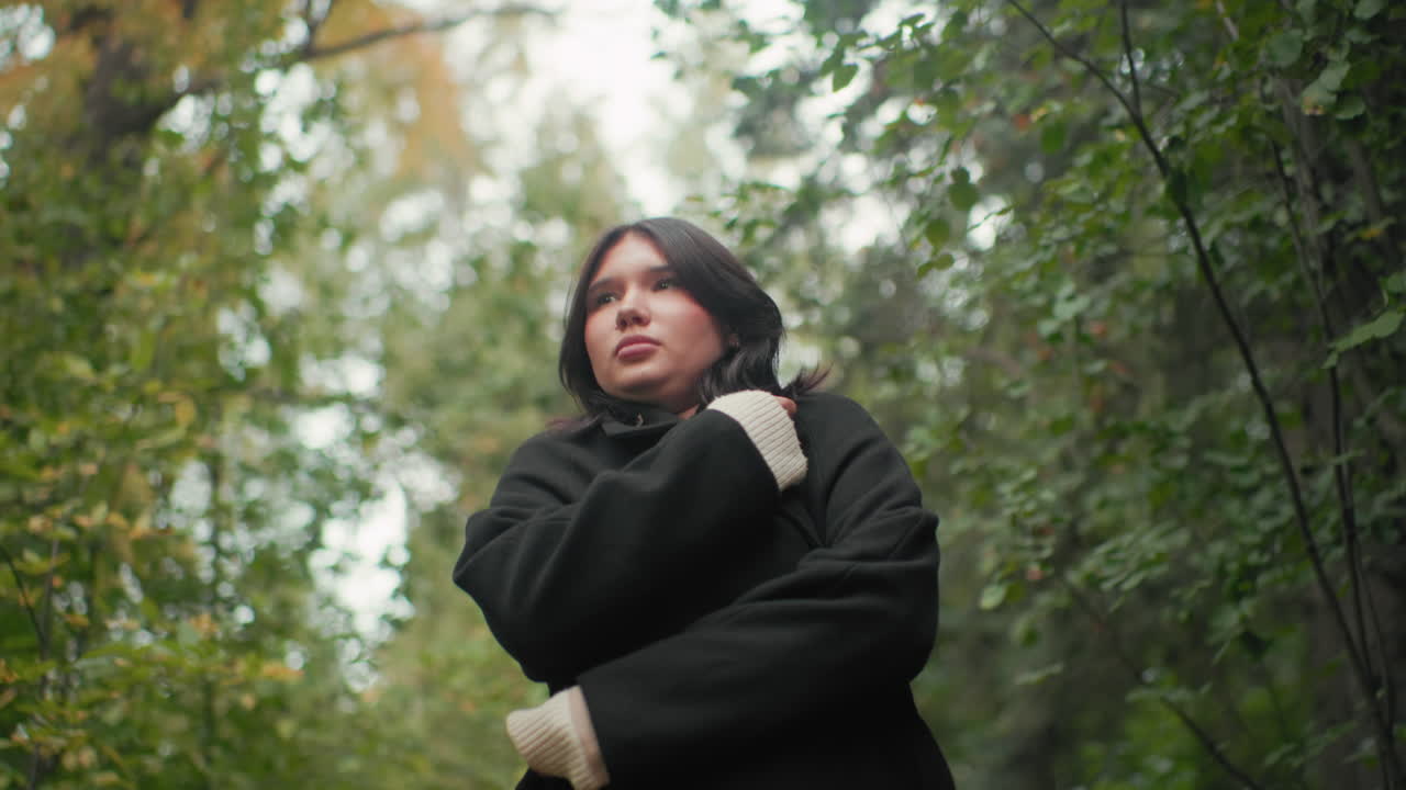 가을에 코트를 여미고 숲길을 거닐면서 담요로 몸을 감싸는 방문객을 올려다본 앵글, 쌀쌀한 날씨, 부드러운 보케 나뭇잎, 나무 사이를 한가롭게 거닐기, 아늑한 움직임