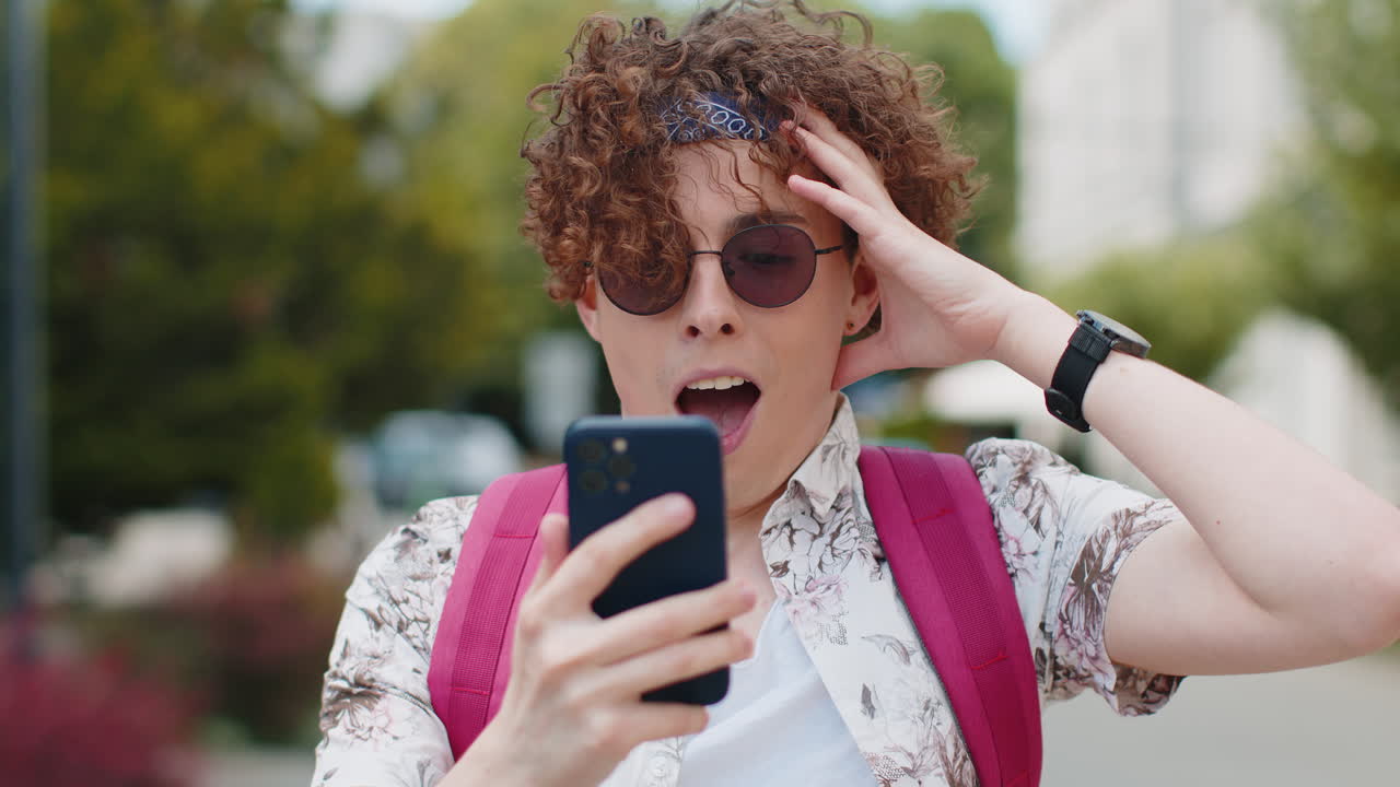 휴대전화를 사용하는 관광객이 승리를 축하하고 좋은 소식을 받습니다. 와우 감정 야외