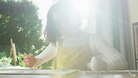 caucasian woman painting at home on sunny day