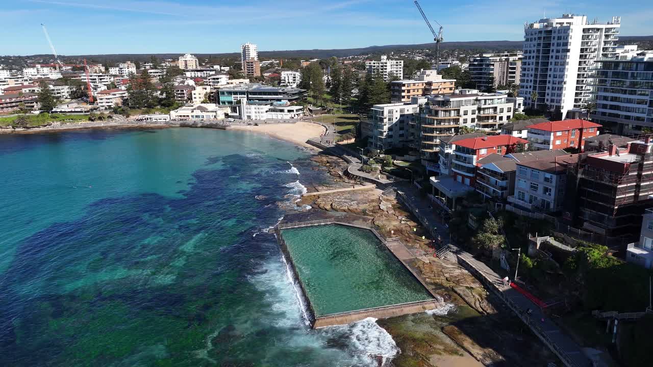 Coastal aerial orbit of Cronulla with oceanfront buildings, waves and clear blue water, Sydney NSW Australia