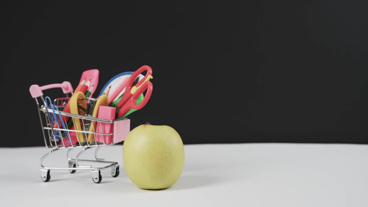 cerrar el carrito de compras con artículos escolares y manzana con espacio de copia en fondo negro