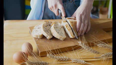 person cutting sliced bread on wooden board with eggs and wheat