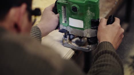 Footage-from-the-shoulder-of-a-craftmans-hands-working-with-polishing-with-manual-grinding-machine-at-wood-workshop.-Grinds-a-large-wooden-plank.-Dust-and-chips-are-scattering-on-the-floor.-Unrecognizable-person.-Slow-motion