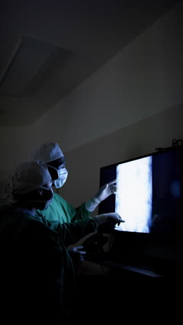 vertical video of diverse surgeons discussing with x-ray scans in operating theatre, slow motion