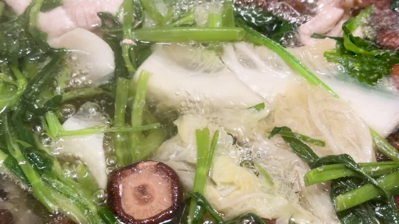 Close-up of traditional Asian hotpot ingredients boiling in broth, with visible steam and vibrant lighting