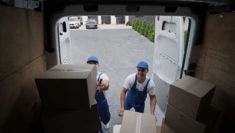 dos jóvenes trabajadores de una compañía de mudanzas están cargando cajas y muebles en un minibus