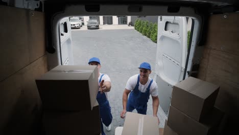 two young workers of removal company are loading boxes and furniture into a minibus