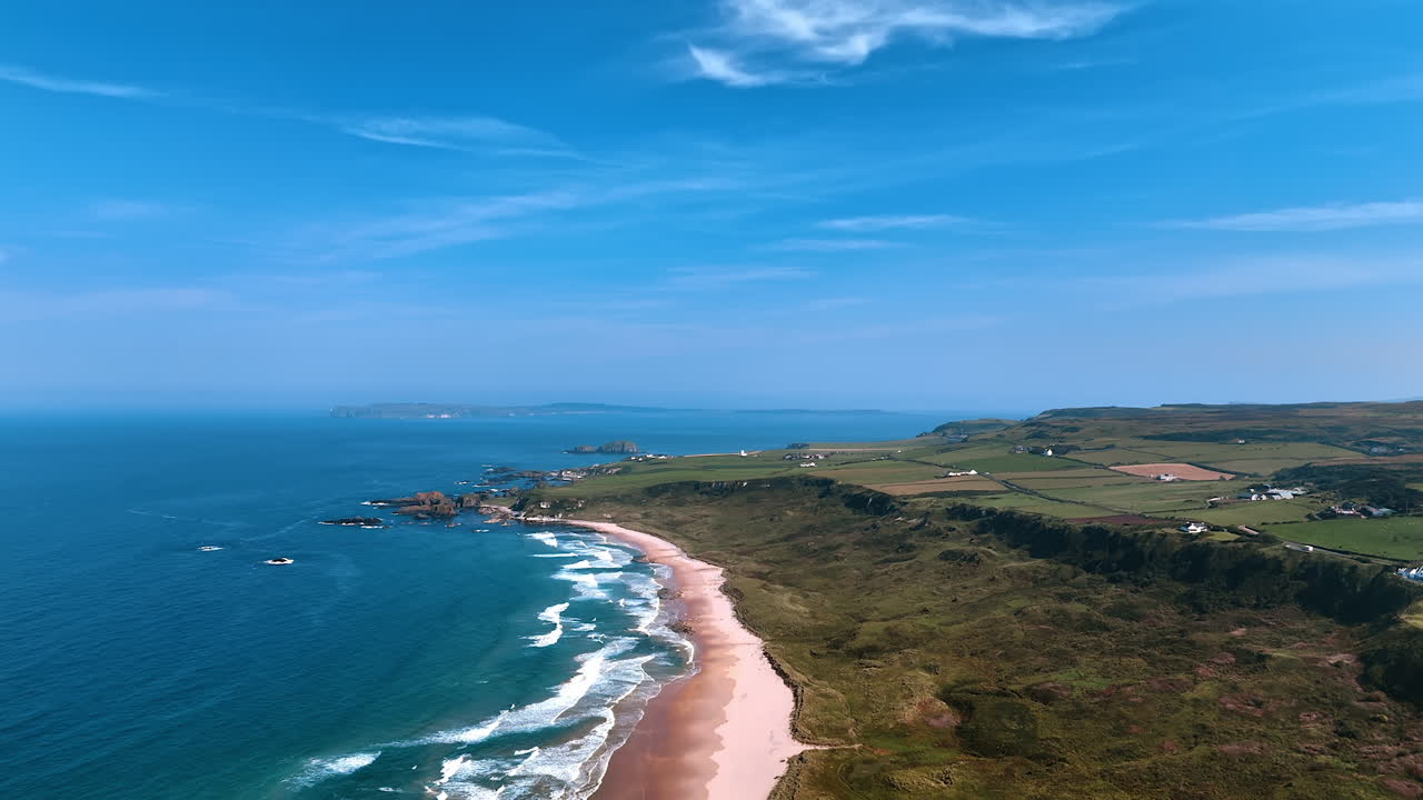 Mesmerizing white waves arrive the narrow sandy beach. Rocky landscape of coastal area of Ireland dwelled by some people. Top view.