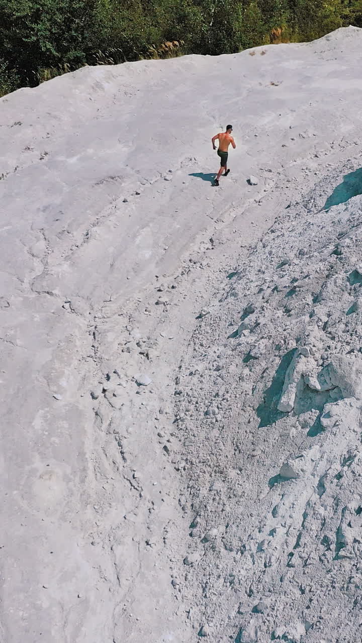 Sportsman in a white canyon exercising. Healthy athlete is running on the rocky hill in a sunny summer day. Aerial view. Vertical video