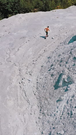 sportsman in a white canyon exercising. healthy athlete is running on the rocky hill in a sunny summer day. aerial view. vertical video