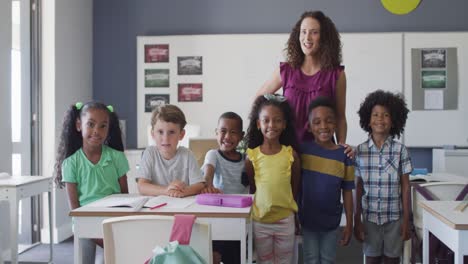 video of happy caucasian female teacher and class of diverse pupils posing at camera