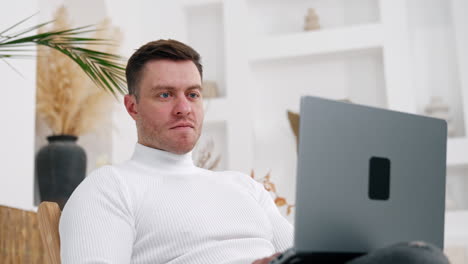 serious caucasian man wearing white shirt looks intently on his laptop. comfortable workplace remote from the office. low angle view.