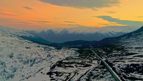 aerial drone backward moving shot over a snow covered country road on mountain plateau surrounded by beautiful norwegian mountain range in the distant