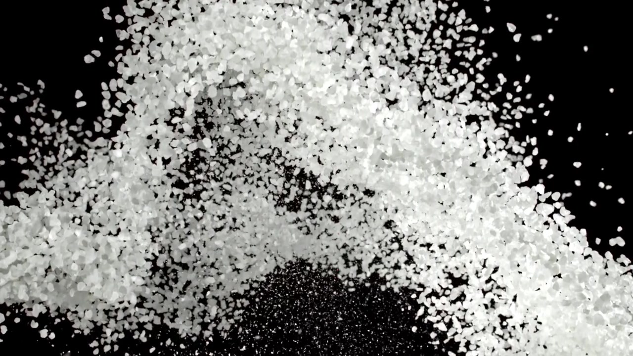 Cristalli di sale bianco che si versano e si diffondono su sfondo nero