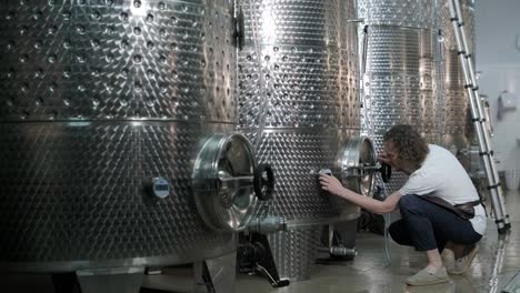 un agricultor o viticultor feliz está caminando en medio de tanques de vino y comprobando un grado de fermentación de la producción de vino de alta calidad en una instalación moderna de elaboración de vino o bodega.
