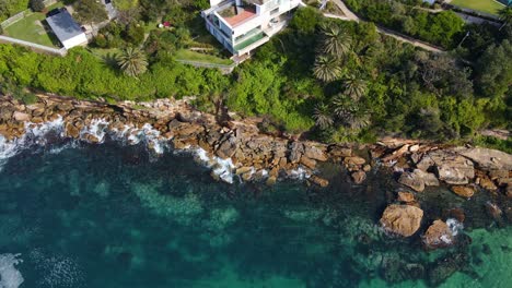 waterfront buildings and hotels with swimming pool - wave hitting the rocky coastline of gordon's bay in sydney, australia