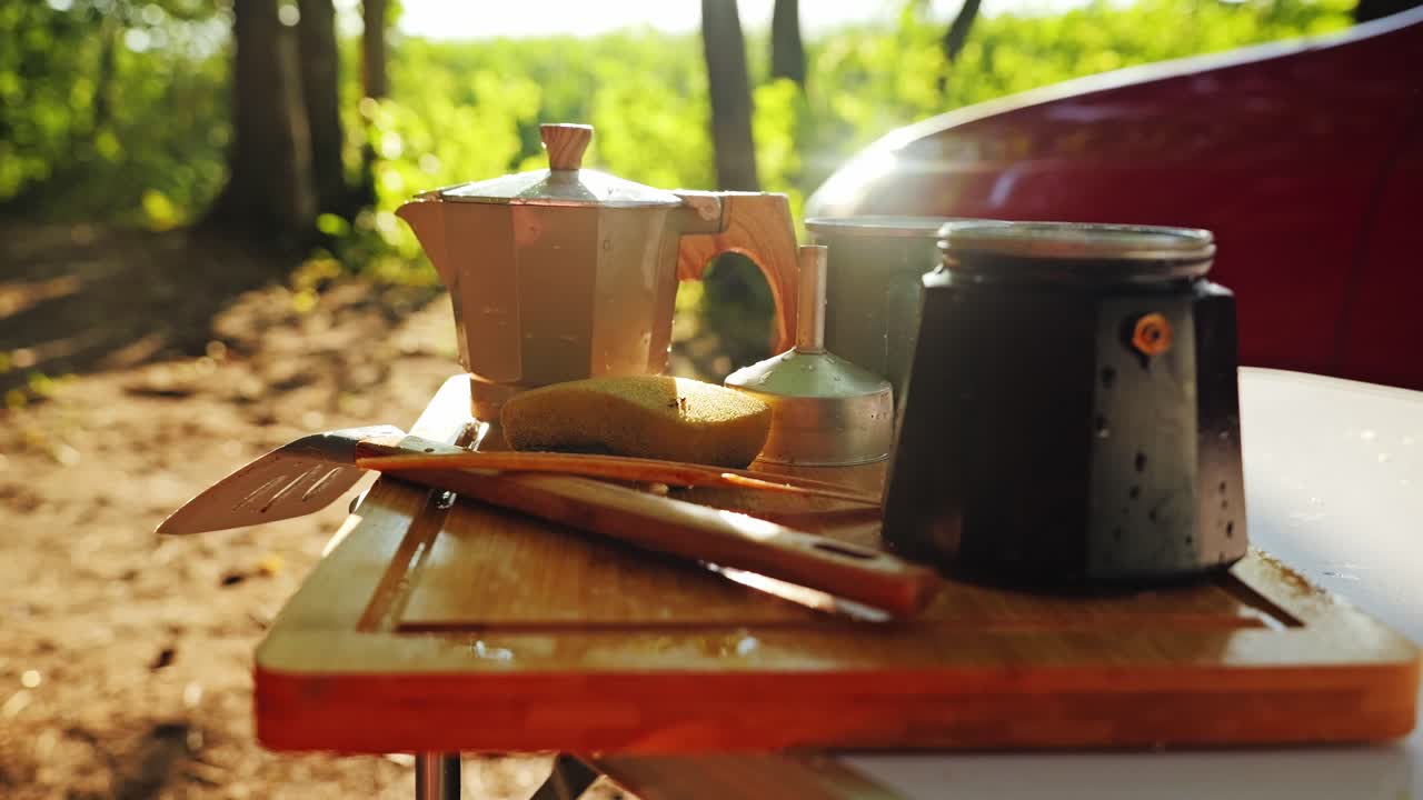 Morning sunlight shines on coffee pot and enamel cups at camping site in Latvia