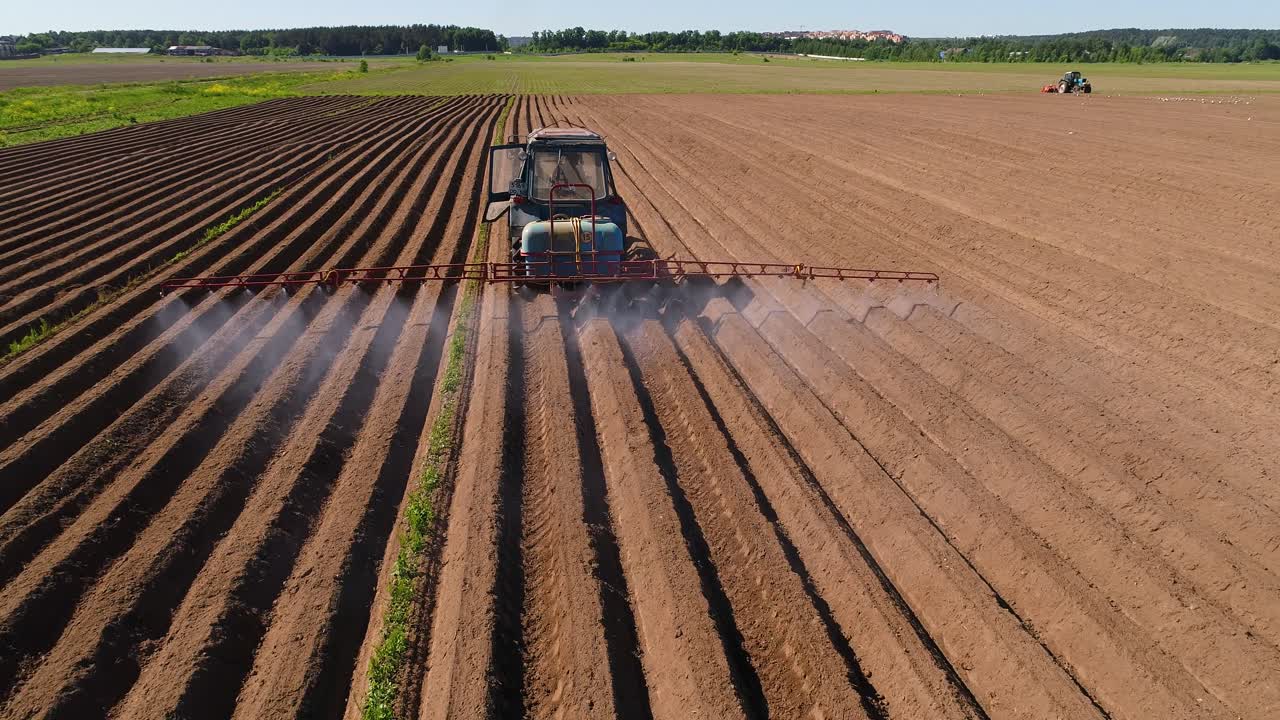 Un contadino su un trattore irrora campi arati con fertilizzanti e prodotti chimici.